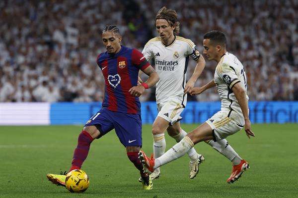 El defensa del Real Madrid Lucas Vázquez (dcha) y el centrocampista croata Luka Modric (c) pelean por el balón con el delantero brasileño del FC Barcelona Raphinha, durante el partido de la jornada 32 de LaLiga EA Sports entre Real Madrid y FC Barcelona, este domingo en el estadio Santiago Bernabéu de Madrid. EFE/Daniel González