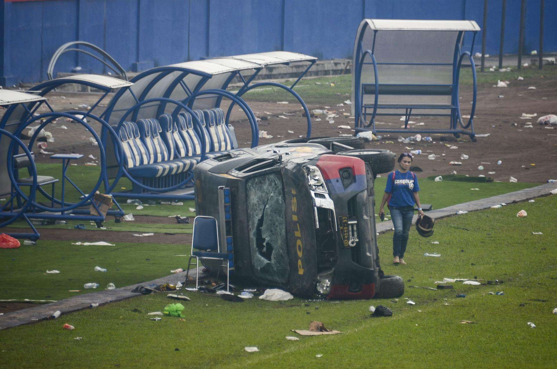 EFE/EPA/SANDI SADEWA/Archivo
INDONESIA FÚTBOL: MALANG, 02/10/2022.- Una mujer pasa junto a un vehículo de la policía destrozado tras los disturbios en un partido de fútbol en el estadio Kanjuruhan de Malang, que han dejado al menos 174 muertos. El brote de violencia se produjo después de que cerca de 3.000 aficionados del equipo Arema irrumpieran en el campo tras la derrota 2-3 sufrida ante el rival Persebaya Surabaya y chocaran con las fuerzas de seguridad, que a su vez utilizaron gases lacrimógenos en un intento de dispersar la multitud. EFE/ Sandi Sadewa